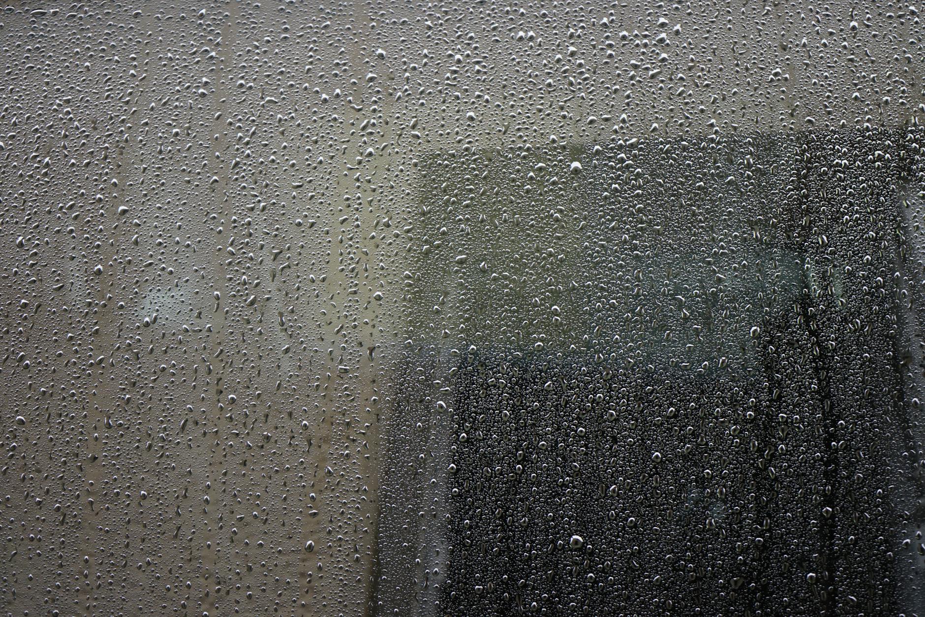 Close-up of a rain-drenched window covered in water droplets, showcasing abstract urban atmosphere.