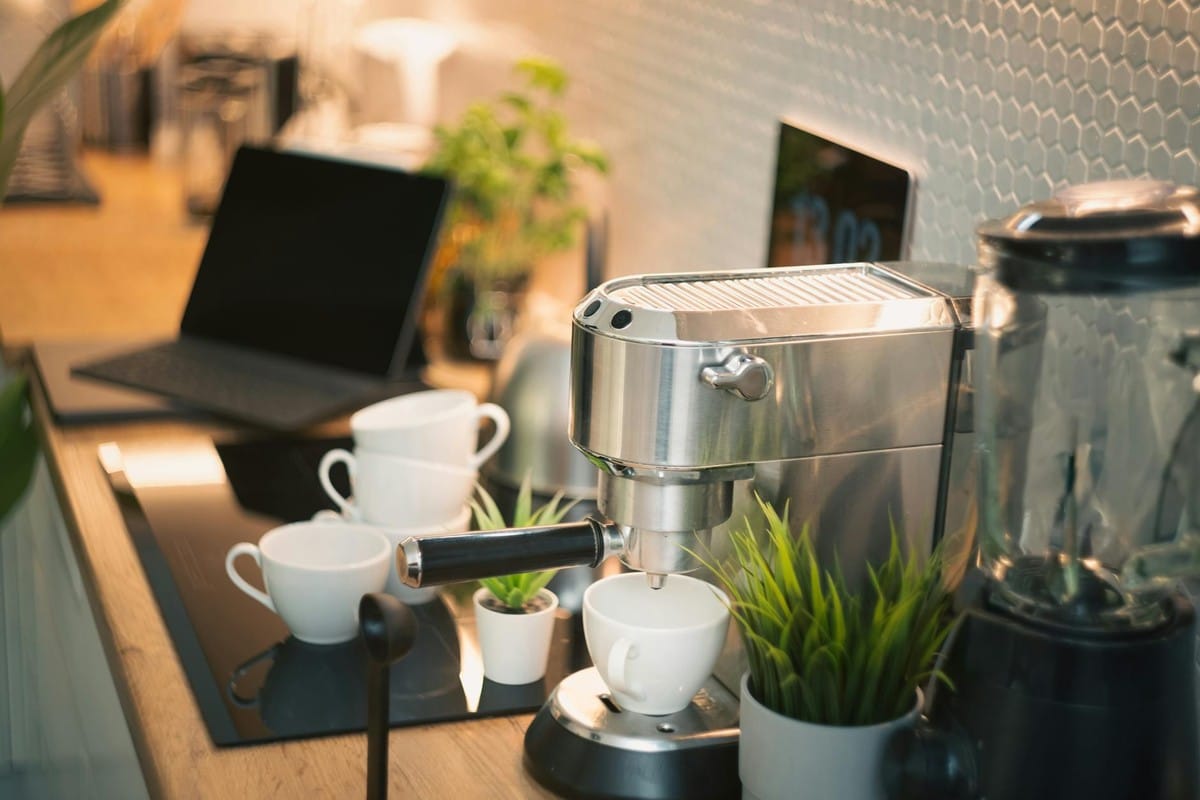 Cozy kitchen counter featuring an espresso machine, laptop, and potted plants in modern design.