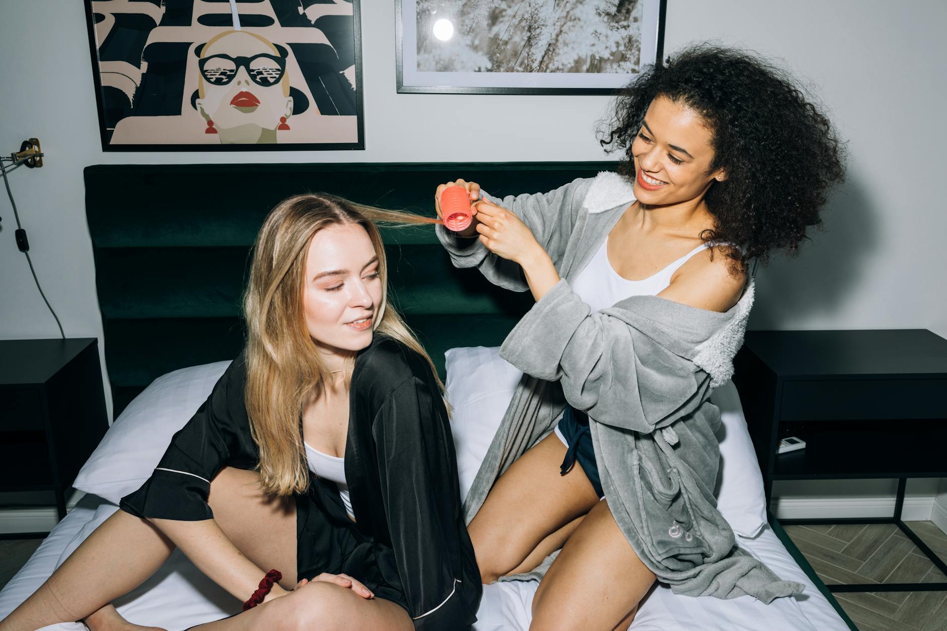 Two young women enjoy a joyful pajama party indoors, styling hair and sharing laughter.